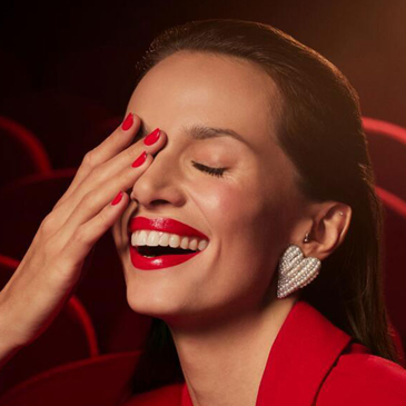 Femme souriante portant un rouge à lèvres rouge et du vernis rouge Bourjois.